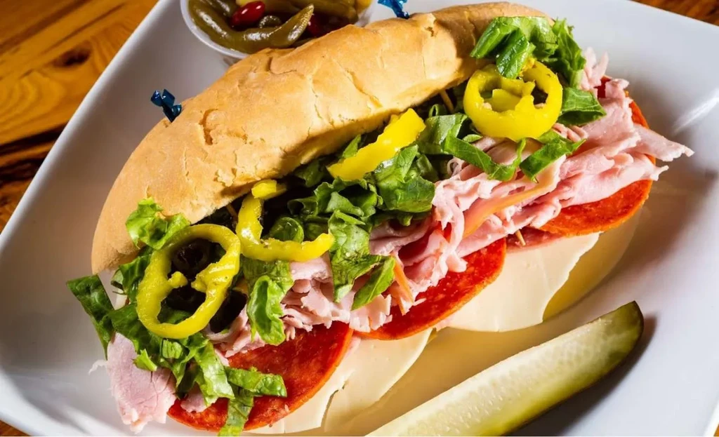 Submarine sandwich with deli meats, cheese, lettuce, banana peppers, and pickle.