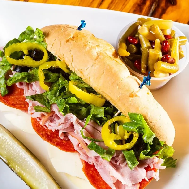 Sub sandwich with deli meats, melted cheese, lettuce, and pickled vegetables.