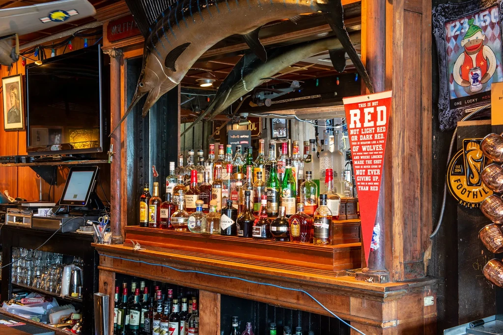 Rustic wooden bar counter with liquor bottles and hanging decorative fish.