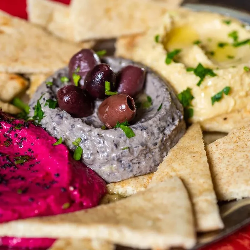 Three colorful dips: beet, olive, and hummus, with pita bread.