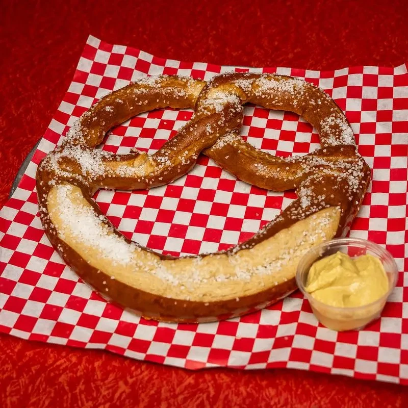 Golden-brown soft pretzel with salt and mustard on checkered paper.