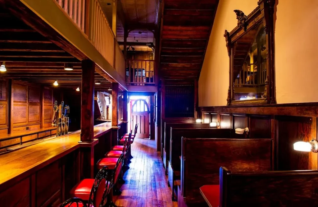 Rustic, warmly lit bar interior with wooden bar, stools, and booths.