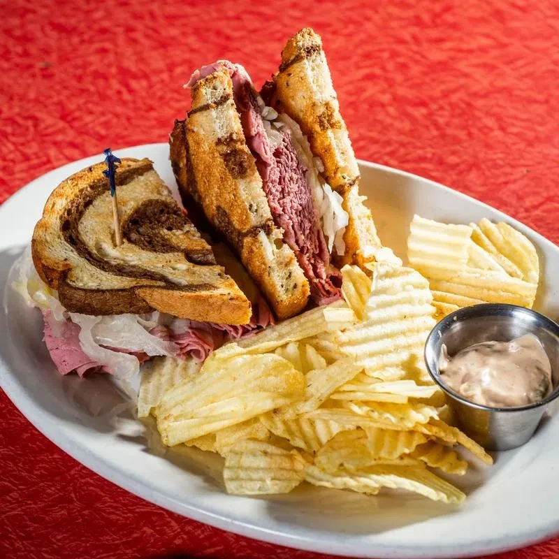 Top-down: Sliced marble rye sandwich with meat, sauerkraut, chips, dip.