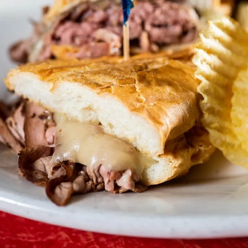 Halved roast beef sandwich with melted cheese and potato chips.