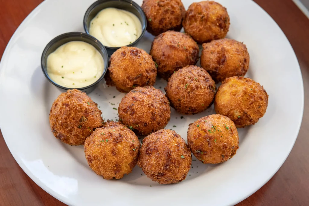 Golden-brown fried appetizer balls garnished with green specks and dipping sauce.
