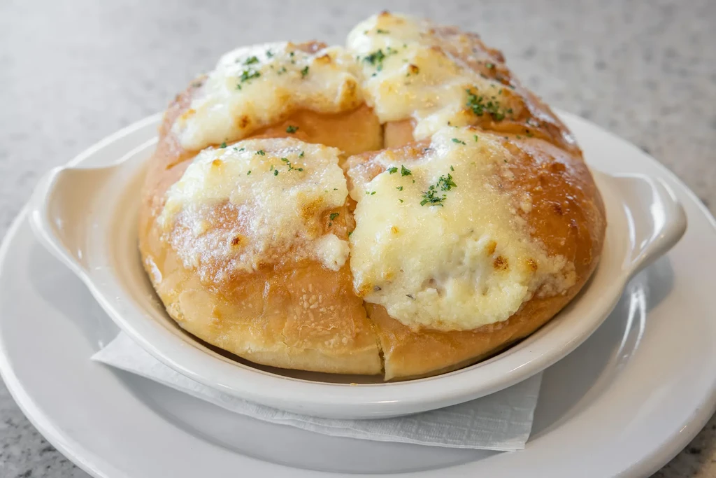 Golden-brown cheesy bread with melted cheese and herbs in a dish.