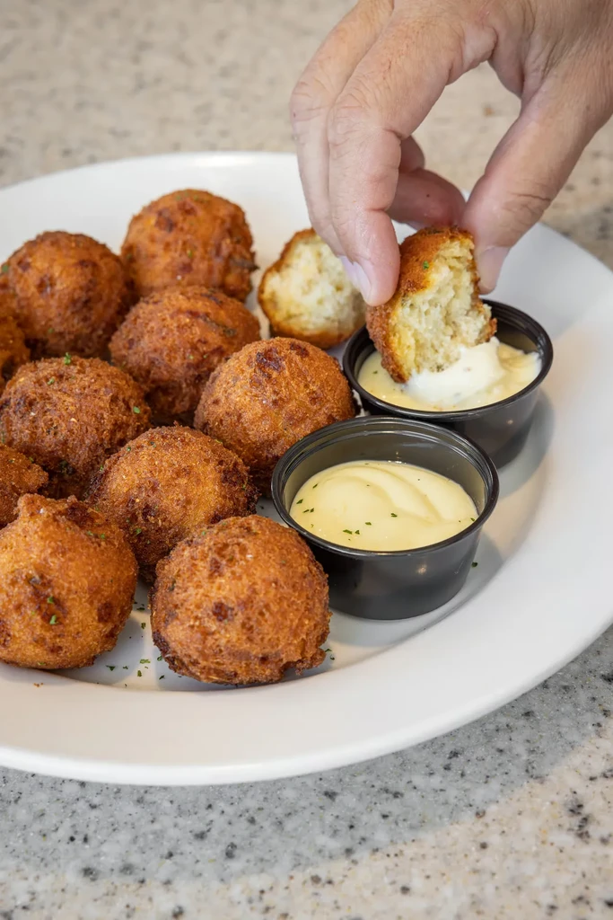 Crispy, golden-brown fritters on a plate; a hand dips one.
