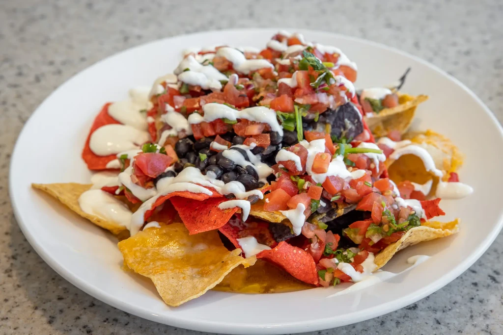 Colorful nachos with chips, beans, tomatoes, creamy sauce, and melted cheese.