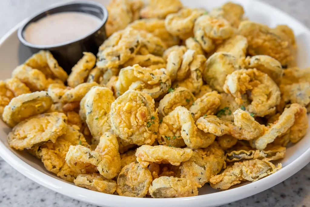Golden-brown fried pickles in a white bowl with dipping sauce.