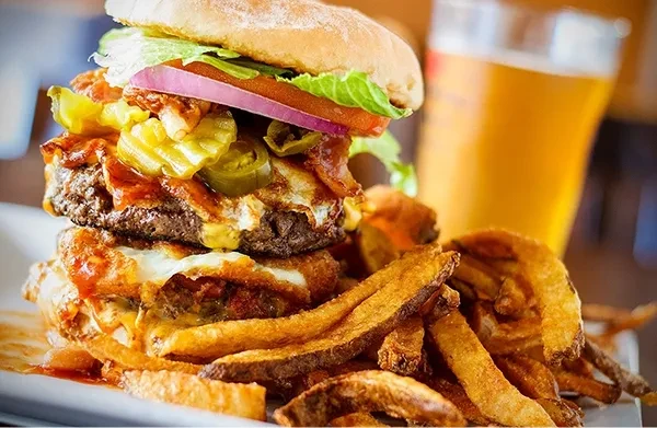 A close-up of a loaded burger, fries, and a beer.
