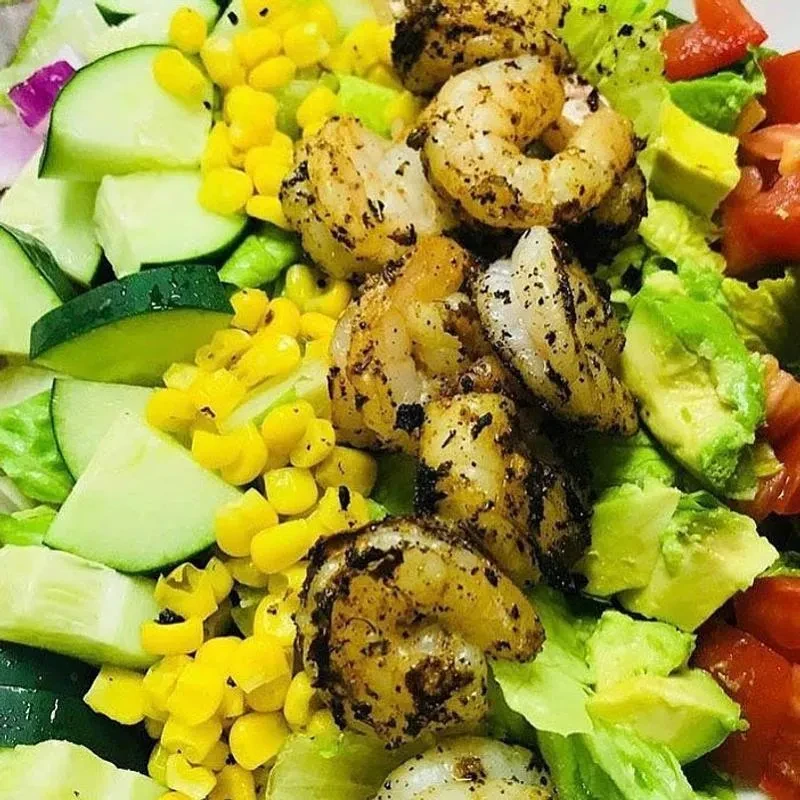 A colorful, close-up shrimp salad with corn, avocado, and tomatoes.
