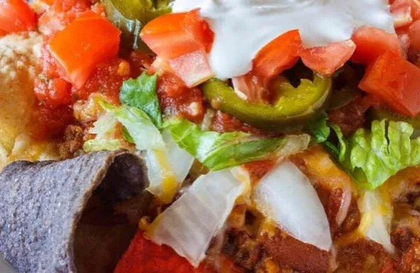 Loaded nachos with meat, melted cheese, fresh toppings, and blue chips.