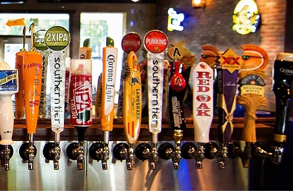 Close-up of a row of diverse, branded beer tap handles in a bar.