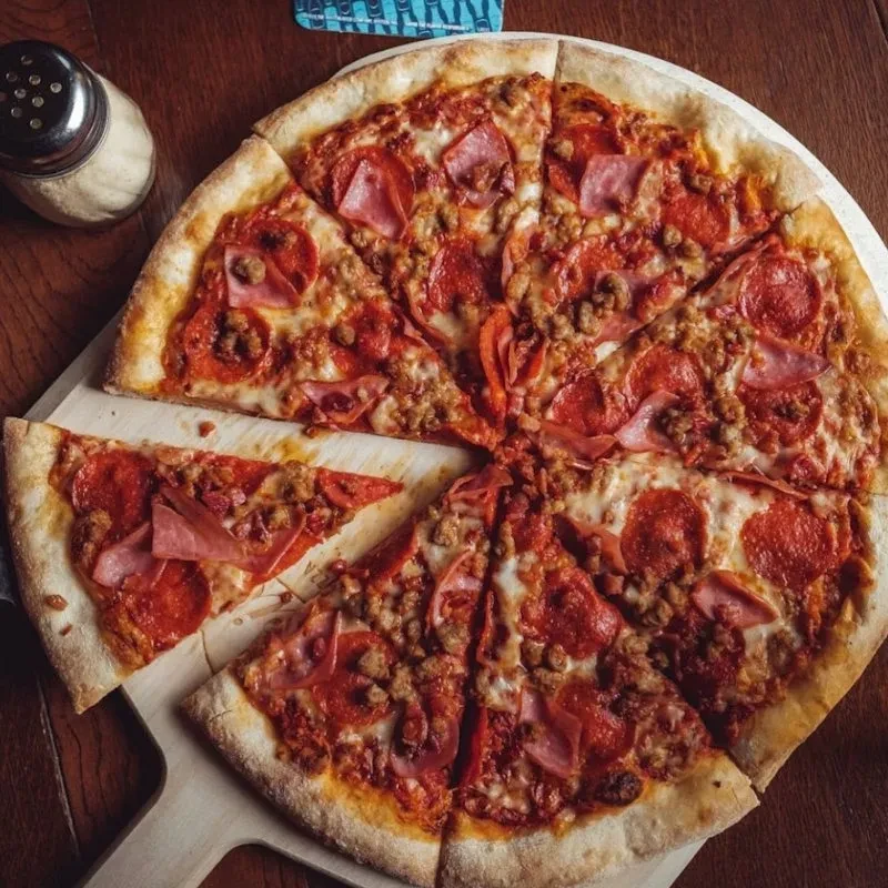 Meat-topped pizza on wooden peel, one slice removed, with Parmesan.