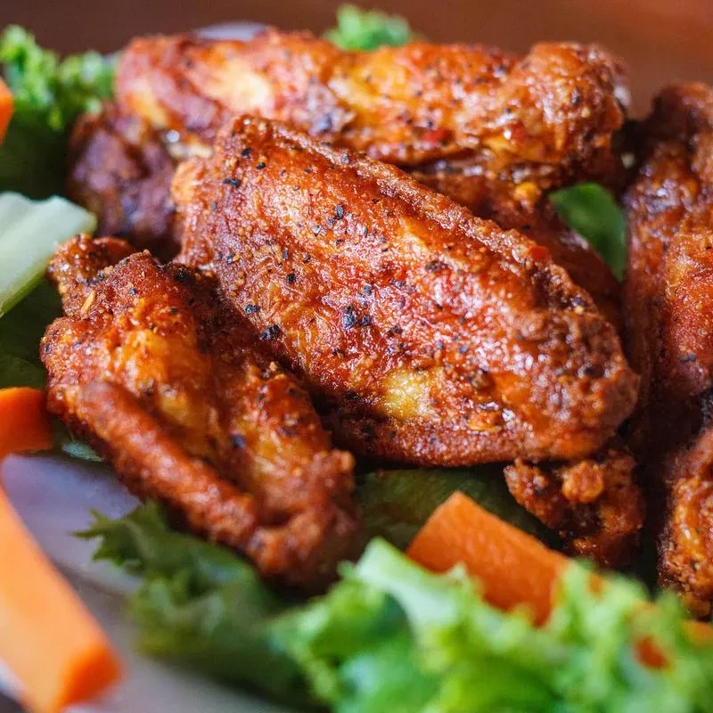 Golden-brown chicken wings with black pepper, garnished with lettuce and carrots.