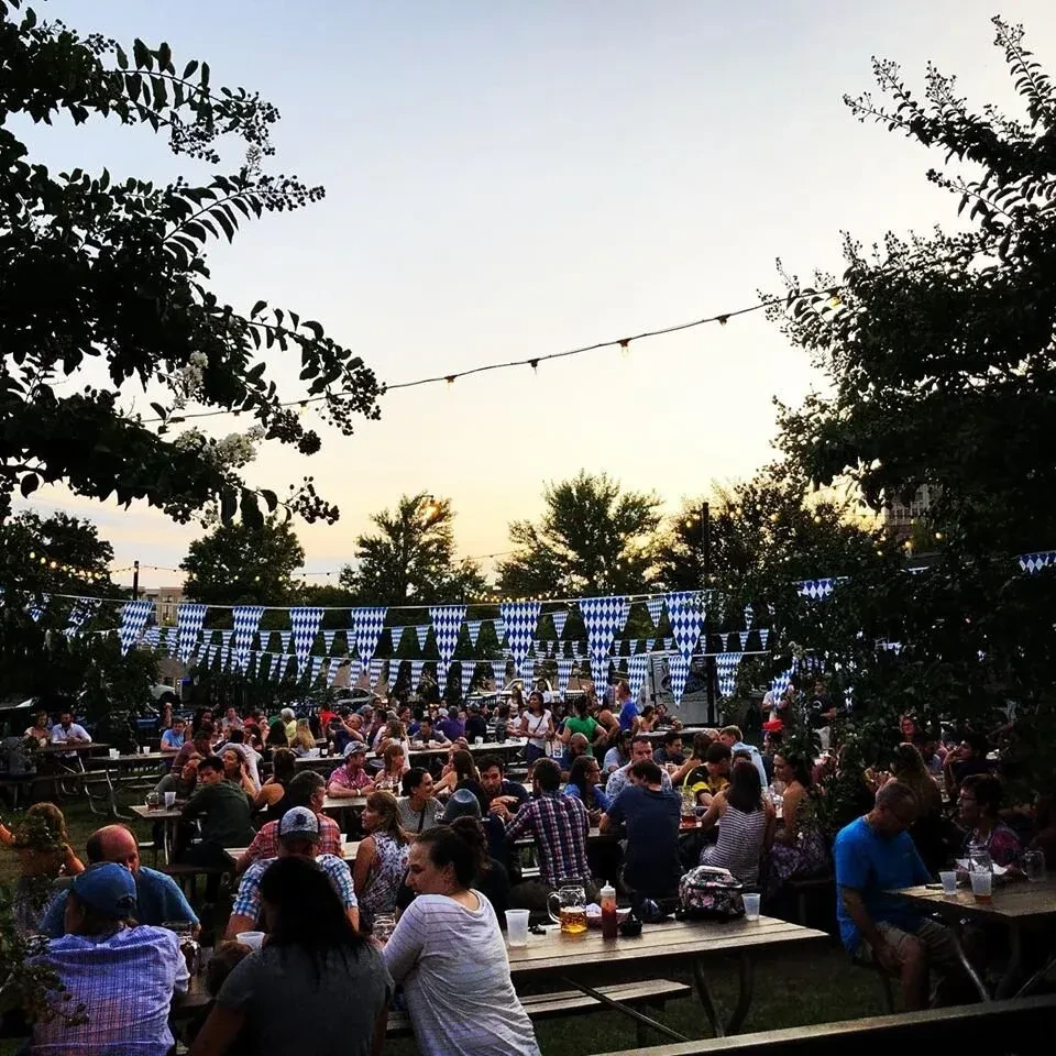 Bustling outdoor beer garden at dusk with people and festive decorations.
