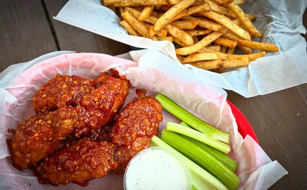 Glistening chicken wings, celery, dipping sauce, and seasoned french fries.