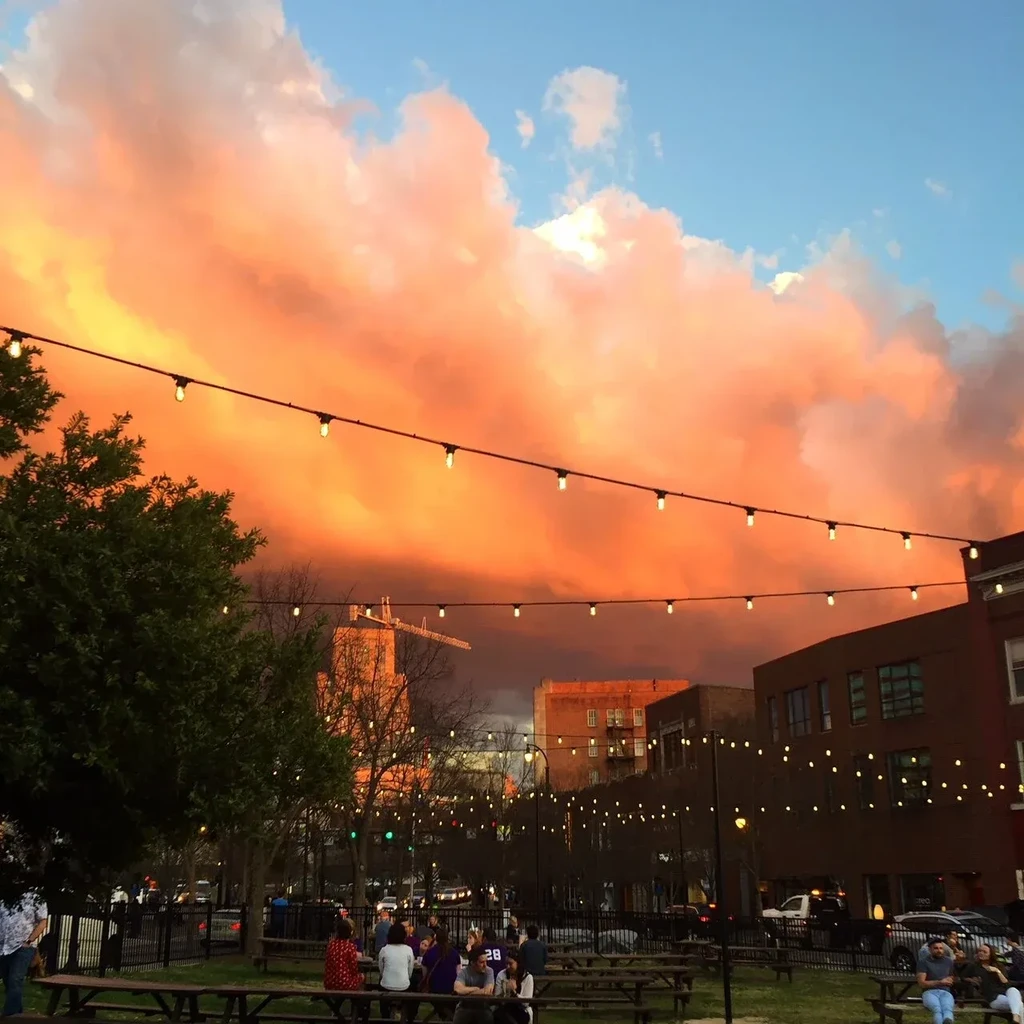 Dramatic sunset over outdoor patio with people and glowing bistro lights.