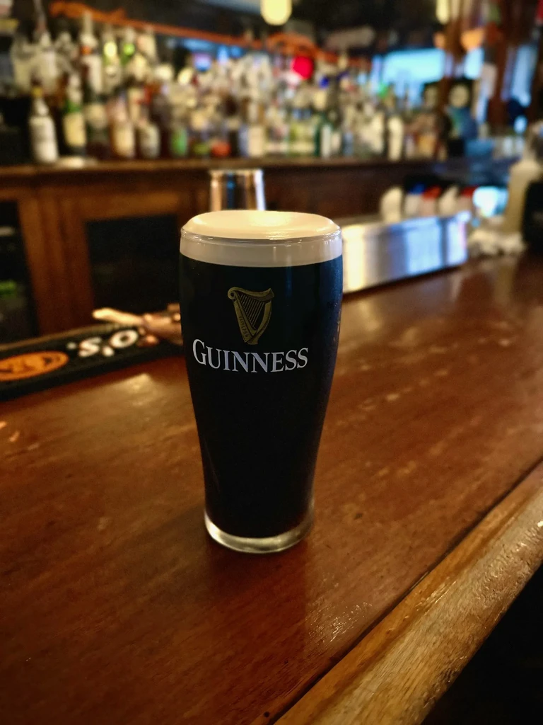 Guinness beer pint with creamy white head on a wooden bar.