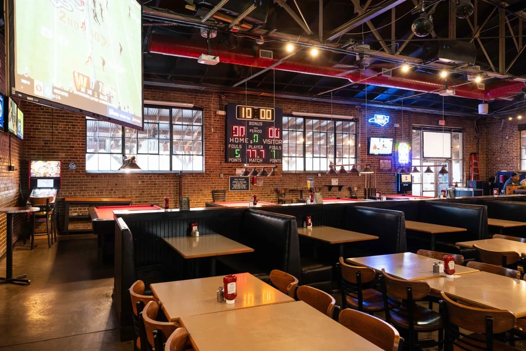 Industrial sports bar with exposed brick walls, multiple screens, and pool tables.