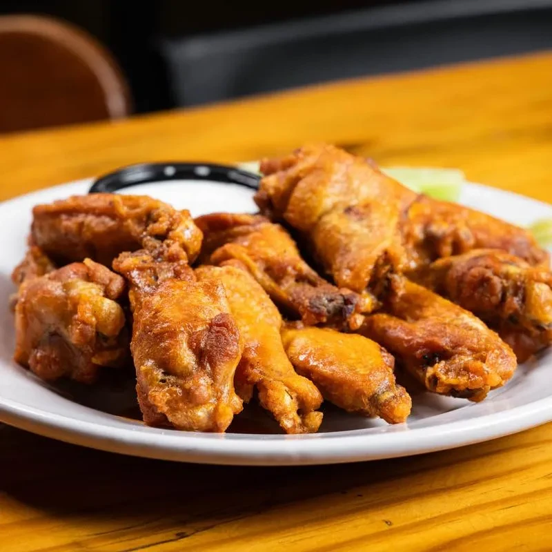 Crispy fried chicken wings on white plate with sauce and celery.