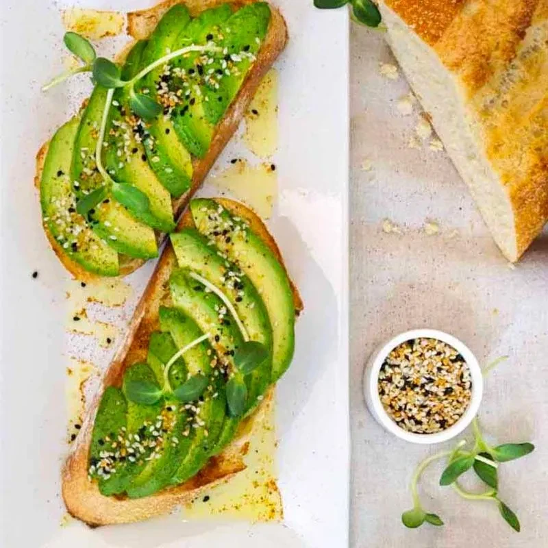 Two slices of avocado toast with everything bagel seasoning on a white plate.