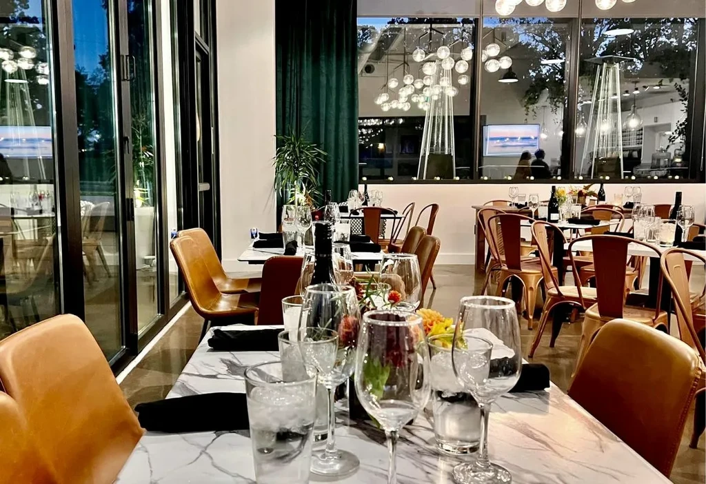 Modern upscale restaurant interior with set marble tables and evening window view.