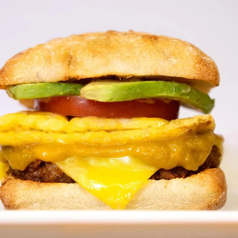 Toasted breakfast sandwich with egg, cheese, meat, avocado, and tomato.