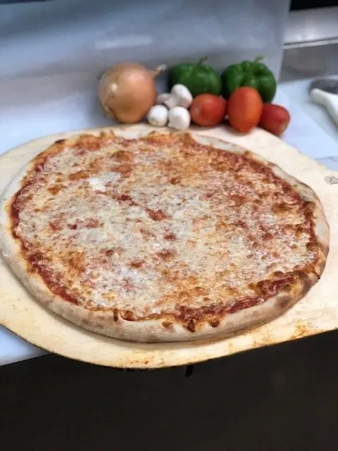 Bubbling cheese pizza on wooden peel with fresh vegetables.