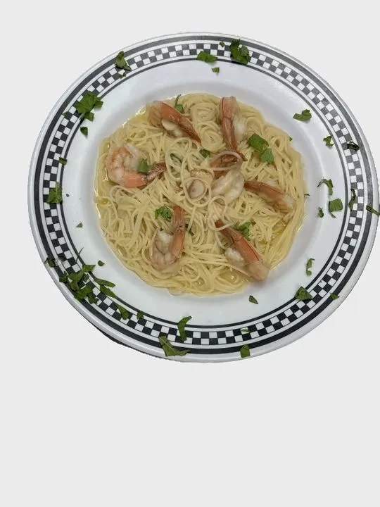 Shrimp pasta on a checkerboard plate, garnished with fresh green herbs.