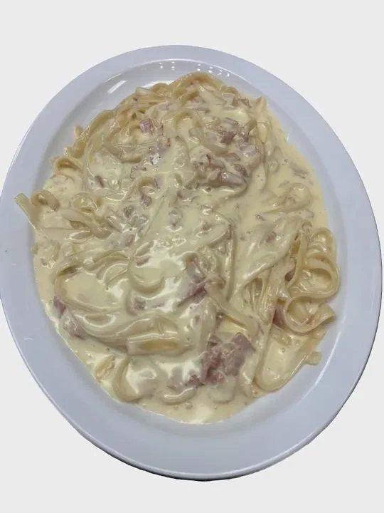 Creamy pasta with ham on a white oval plate.