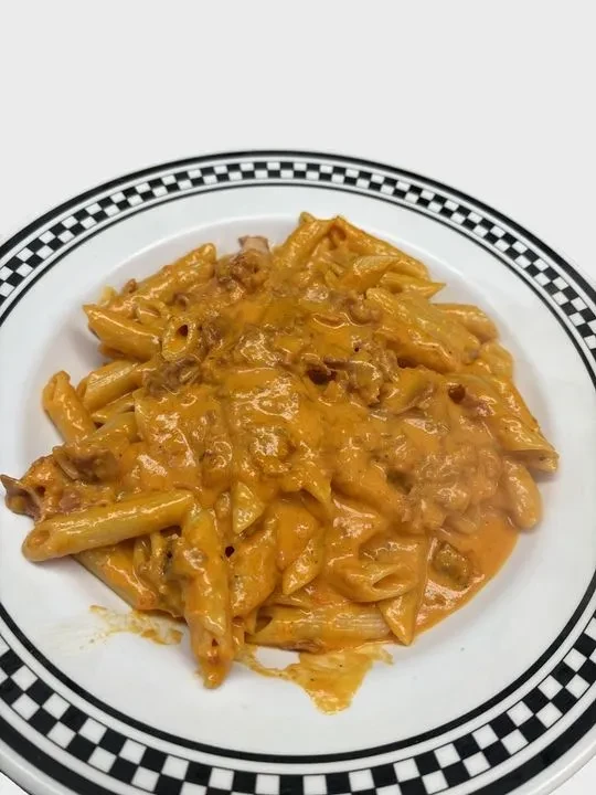 Overhead penne pasta with creamy orange-red meat sauce, checkerboard plate.