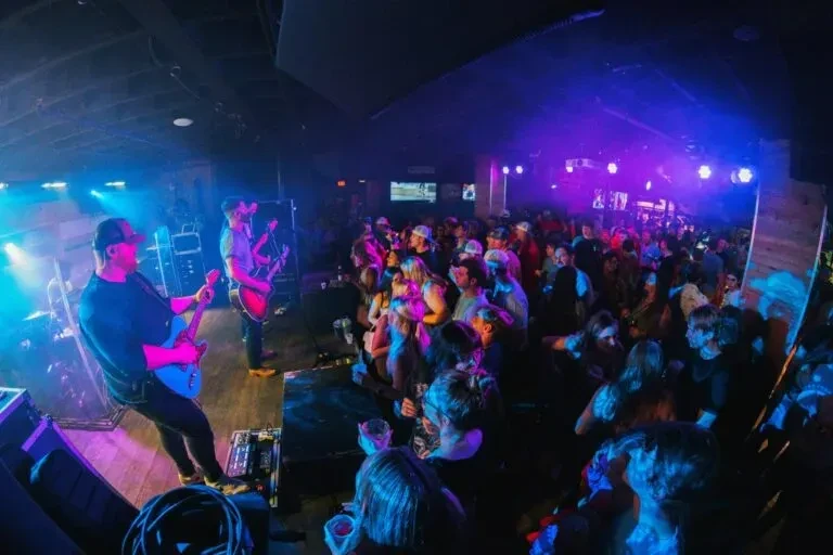 Vibrant stage lights illuminate a band performing for an engaged crowd.