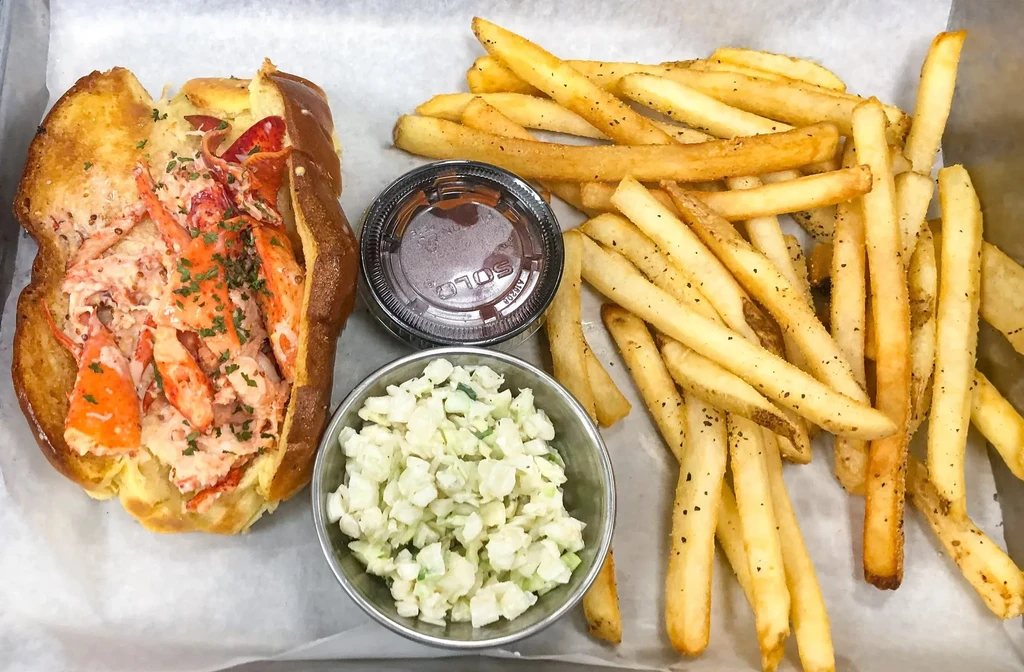 Overhead view of a lobster roll, french fries, coleslaw, and dipping sauce.