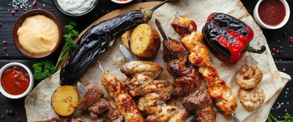 Overhead shot of grilled kebabs, roasted vegetables, and various sauces.