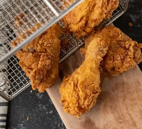 Glistening, crispy golden-brown fried chicken on a wooden board.