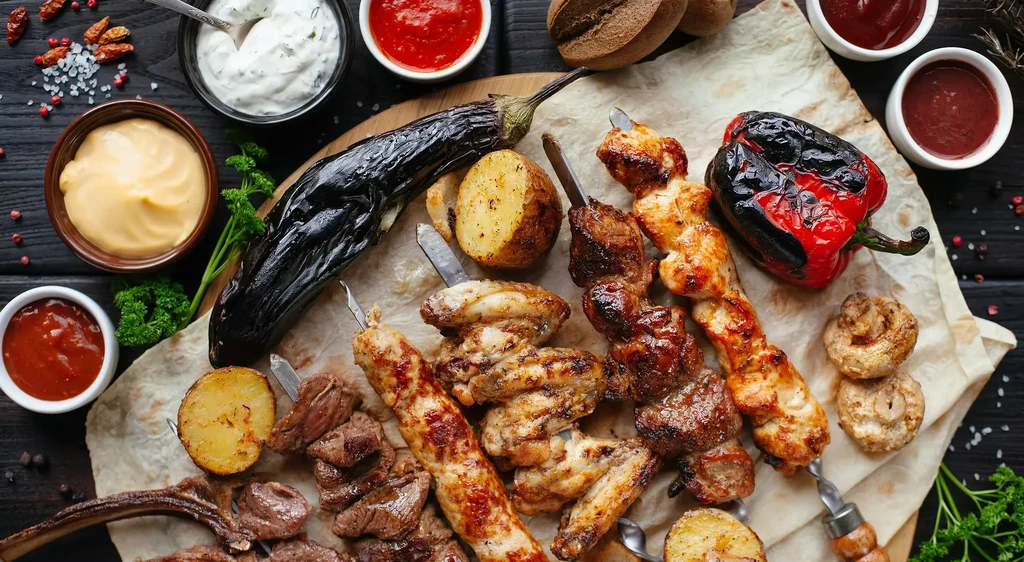 Platter of grilled meats, vegetables, and sauces on a wooden board.