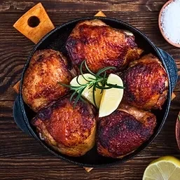 Five roasted chicken pieces with rosemary and lemon in a cast-iron pan.