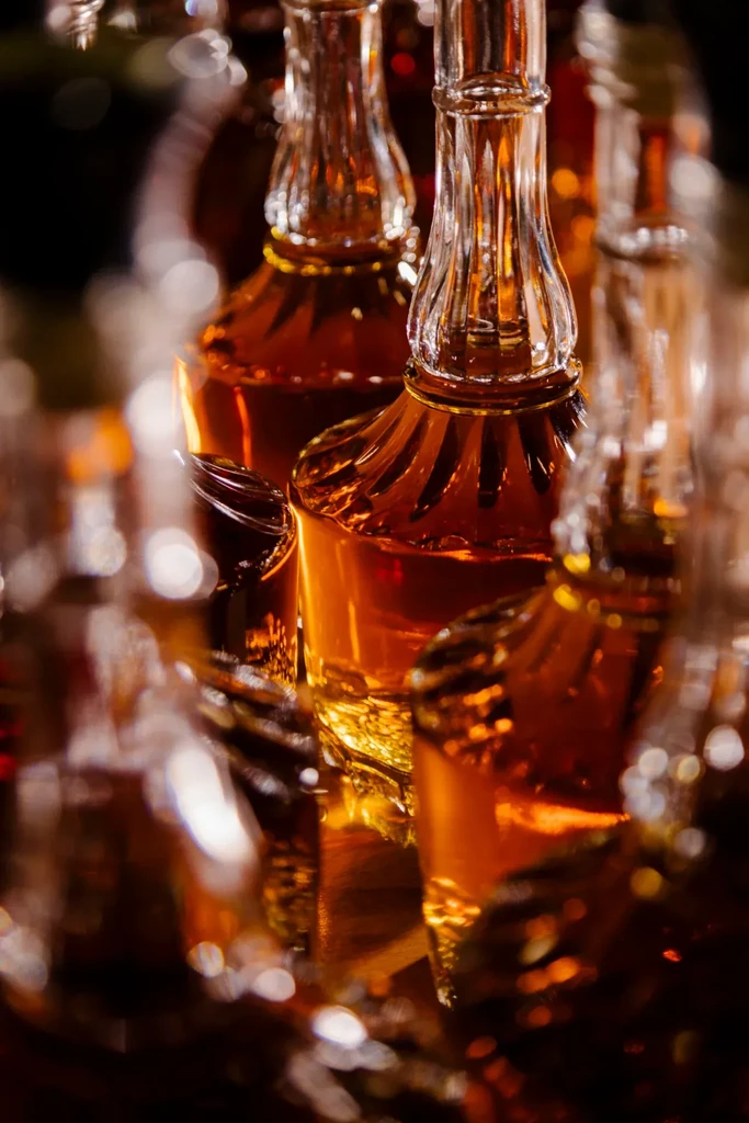 Ornate glass bottles of glowing amber whiskey on dark background.