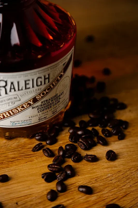Raleigh Society coffee-cask bourbon bottle with scattered coffee beans.