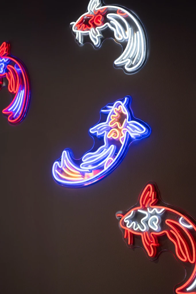 Neon light installations of stylized koi fish on a dark wall.