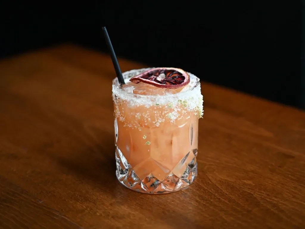 Peachy-orange cocktail in faceted glass, crusted rim, dried blood orange.