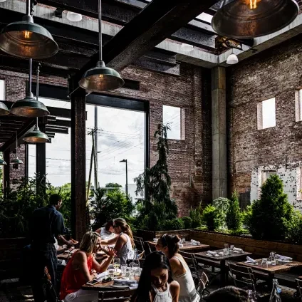 Industrial-chic restaurant interior with brick, plants, windows, and diners.