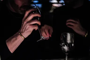 Bearded hands hold wine glass, smelling wine in sophisticated setting.