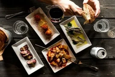 Top-down view of a rustic table with tapas, drinks, and interacting hands.