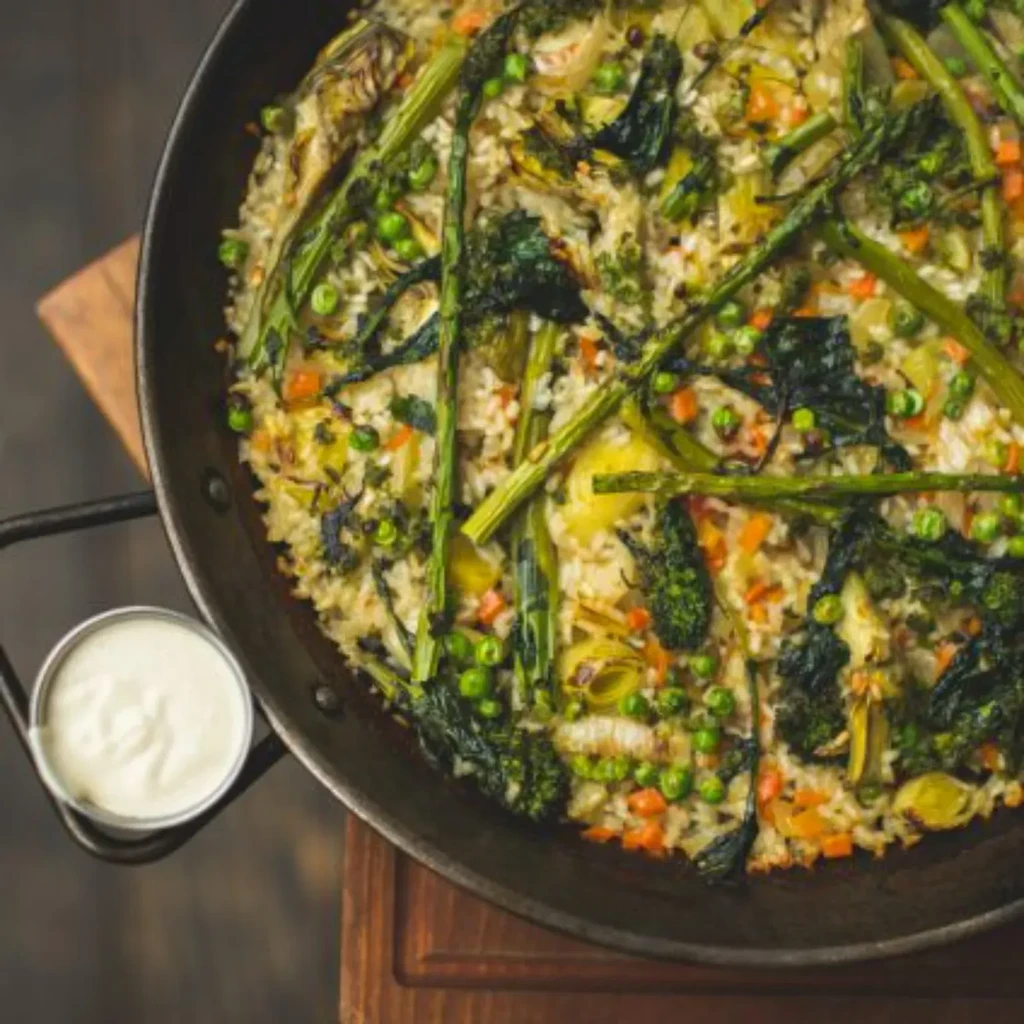 Dark pan of vibrant rice and roasted vegetables with dipping sauce.
