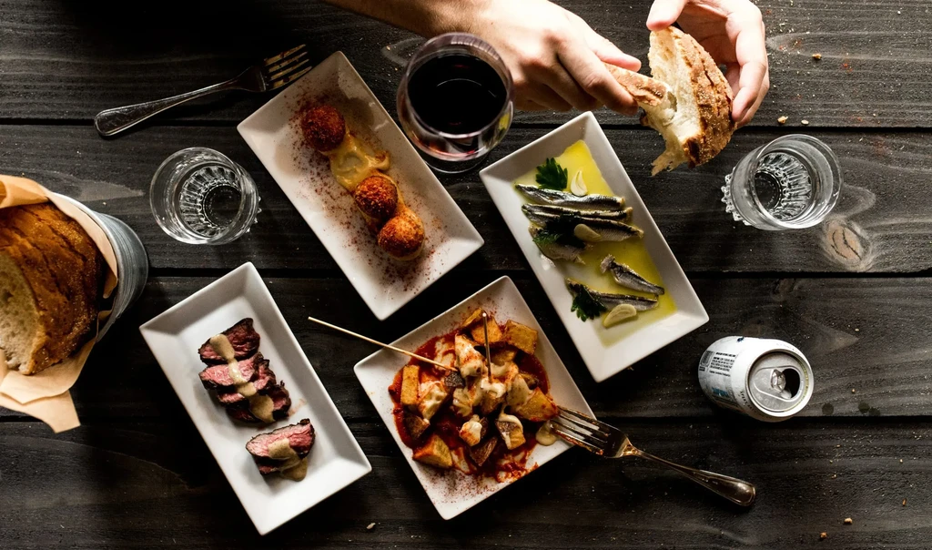 Tapas-style dishes, bread, and wine on a rustic wooden table.