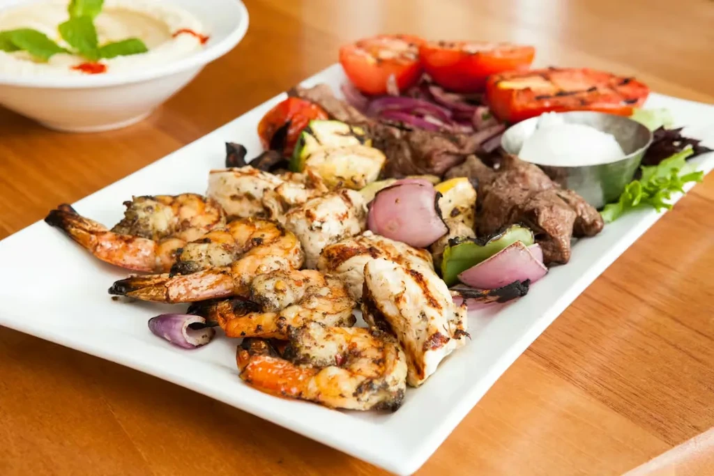 Platter of grilled shrimp, chicken, beef, vegetables, and dipping sauce.