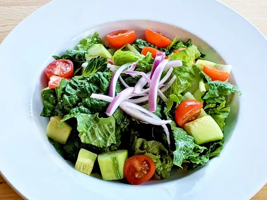Fresh salad with lettuce, tomatoes, cucumbers, and red onions in white bowl.