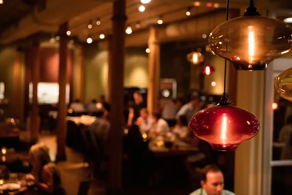 Two glowing pendant lights illuminate a warm restaurant with blurred patrons.